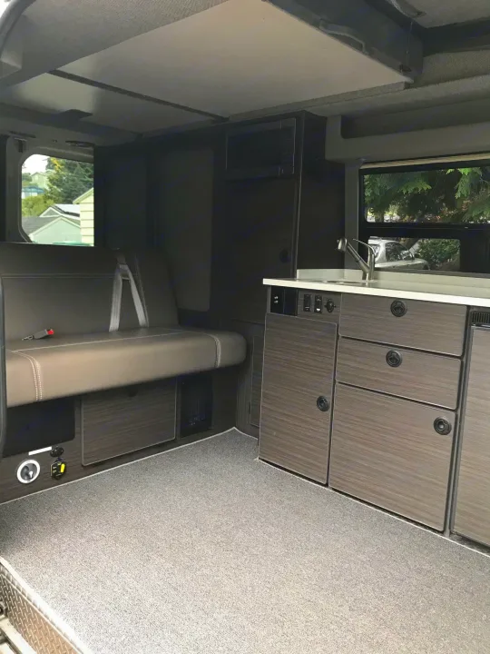 Inside this modern **rv rental**: a comfortable bench seat, compact kitchen with sink, microwave, and stylish dark cabinets.. Mercedes Sprinter 2018