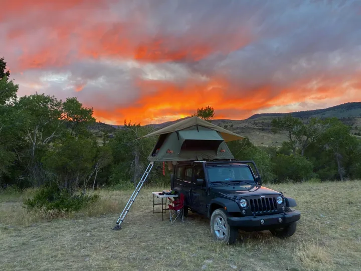 Jeep Wrangler with a rooftop tent set up at golden hour, a great RV rental alternative for camping.. Jeep Wrangler Unlimited 2018