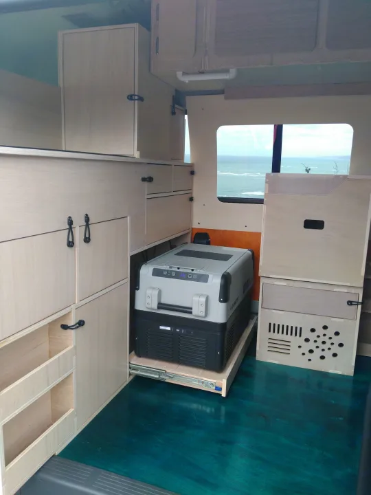 RV rental with light wood custom cabinetry, a pull-out fridge, and vibrant teal floor, offering an ocean view.. Toyota Hiace 2006