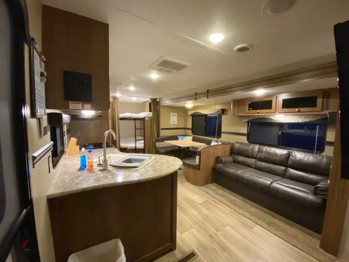 Spacious RV rental interior: kitchen, dining booth, sofa, and bunk beds create a comfortable living area.. Dutchmen Aspen Trail 2018