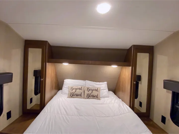 Cozy RV rental bedroom with a fresh white bed, built-in storage, and ambient lighting. Ideal for travel comfort.. Dutchmen Aspen Trail 2018