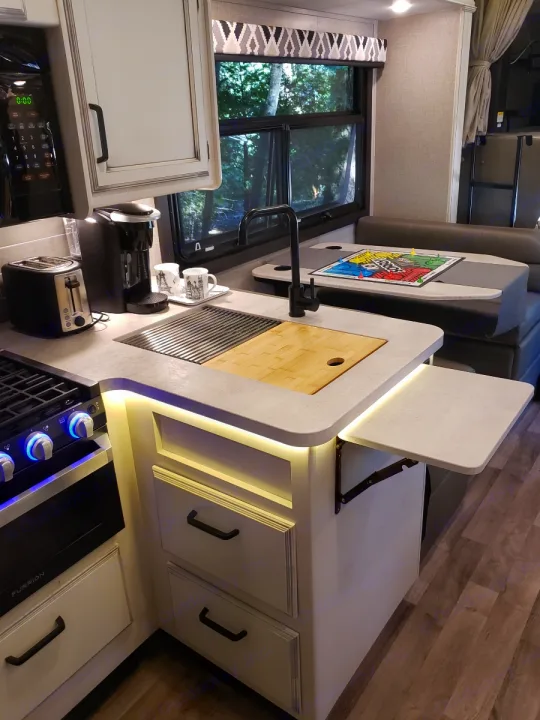 Modern RV rental kitchen with compact amenities, dinette, and bright under-cabinet lighting, perfect for travel comfort.. Jayco Greyhawk 2021