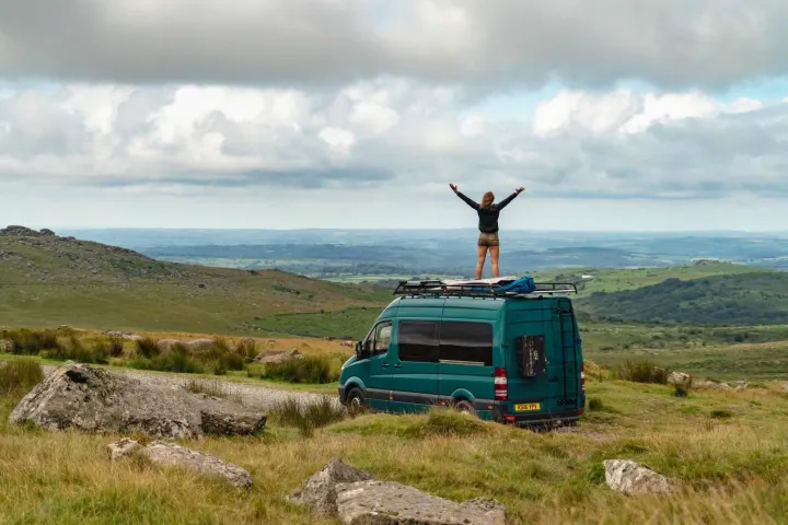 Embrace freedom! A person on an RV rental van views sweeping green landscapes under cloudy skies, arms outstretched.. Mercedes-Benz Sprinter 2016