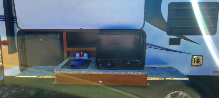 This RV rental features an outdoor kitchen with a pull-out counter, mini-fridge, sink, and two-burner stove.. Keystone Passport 2016