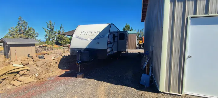 Passport travel trailer (RV rental) parked outdoors on a gravel lot between a shed and large metal building.. Keystone Passport 2016