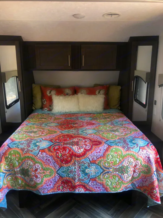 Cozy RV rental bedroom featuring a queen bed, colorful quilt, pillows, built-in cabinets, and side windows.. Forest River Evo 2019