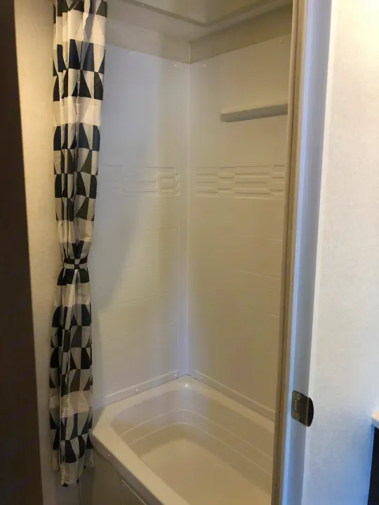 Compact RV rental bathroom with a clean white shower/tub combo and a modern geometric shower curtain.. Forest River Evo 2019