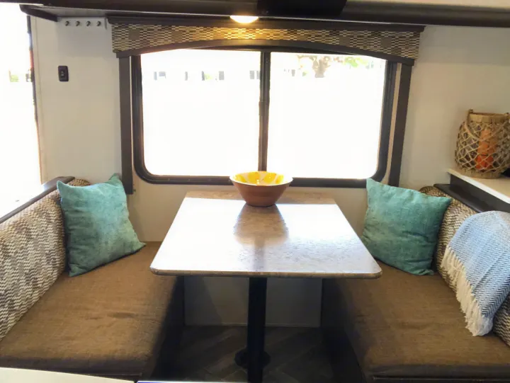 Experience our comfortable RV rental. This cozy dinette features a table, bench seating, pillows, and a large window.. Forest River Evo 2019
