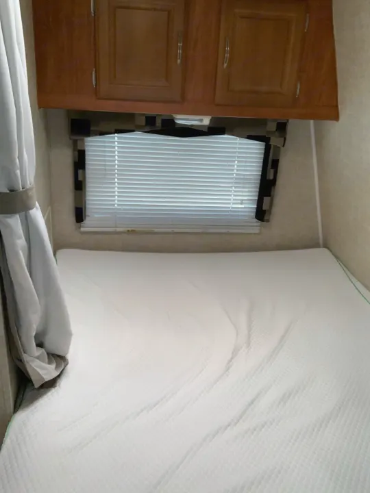 RV rental bedroom interior with a white mattress, window, and wood cabinets for a compact sleeping space.. ForestRiver Sandstorm 2008