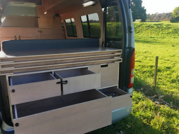 Custom-built wood interior of an RV rental, showcasing clever storage drawers & pull-out bed system.. Toyota Hiace 2006