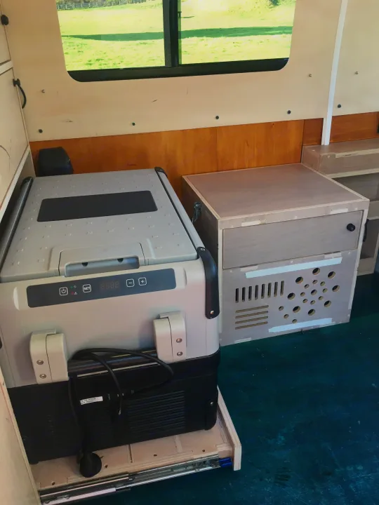 Inside an RV rental: a portable fridge on a pull-out tray and a custom wooden cabinet, perfect for camping trips.. Toyota Hiace 2006