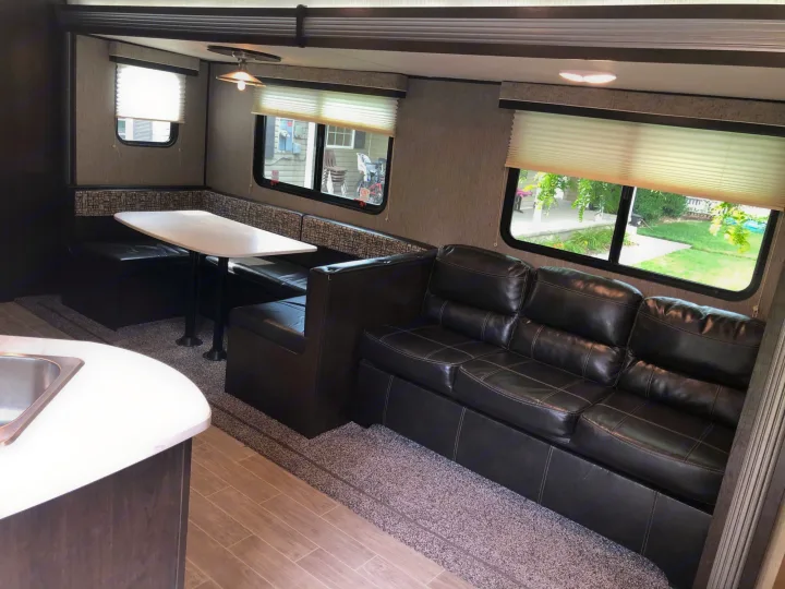 Interior of an RV rental: includes a dinette with booth seating, a spacious sofa, and kitchen counter visible. Ideal for journeys.. Heartland Trail Runner 2020
