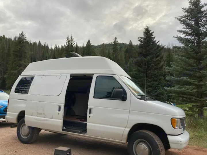 Spacious white high-top camper van, an ideal RV rental for exploring forests. Open door shows cozy interior for van life.. Ford E350 Box Van 1997