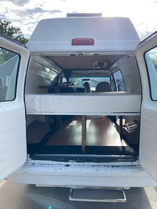 RV rental camper van interior. Features a convertible bed/bench, built-in storage, and visible front cab, ready for travel.. Ford E350 Box Van 1997