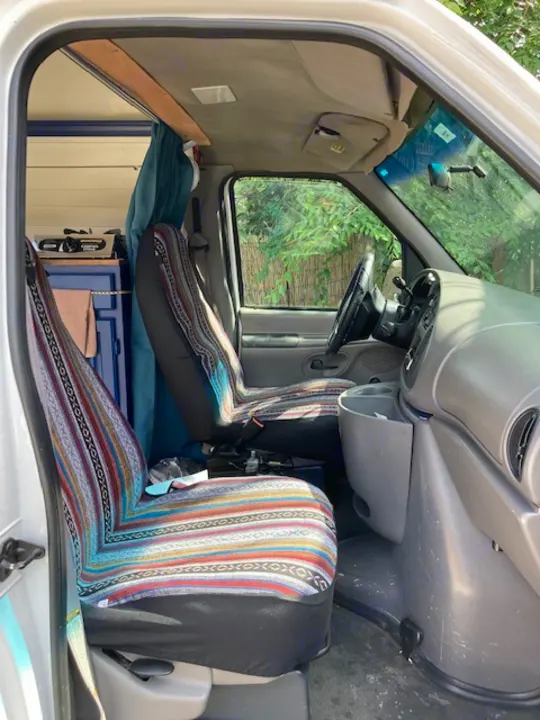 RV rental van interior, showing colorful patterned front seats and a custom bed area behind for travelers.. Ford E350 Box Van 1997