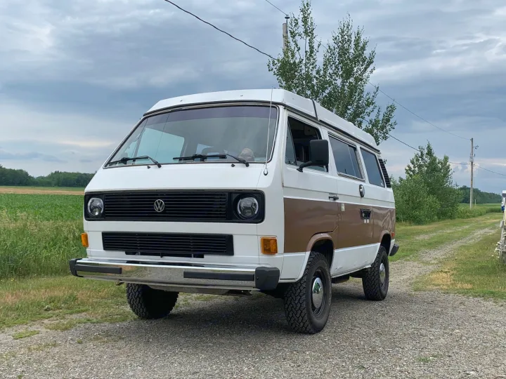 A two-tone white and brown VW van on a gravel road under a cloudy sky.. Volkswagen T3 Westfalia 1984