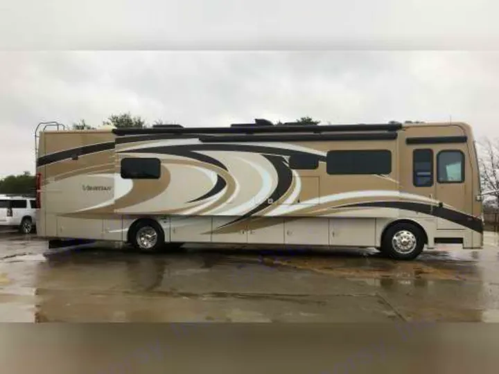Luxury RV rental. A large beige Tiffin Ventana motorhome with black/white graphics parked on wet pavement under an overcast sky.. Thor Motor Coach Venetian 2016