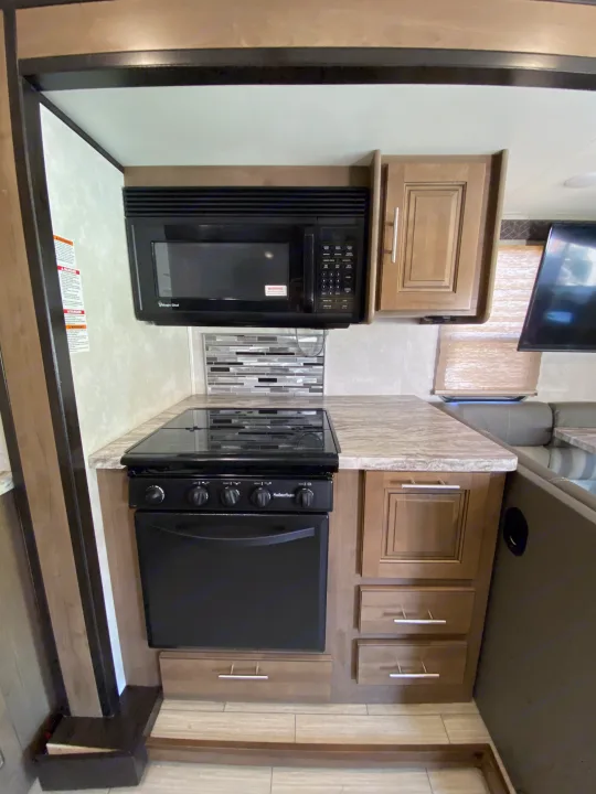 Modern RV rental kitchen with dual built-in ovens/microwaves, ample cabinet storage, and tiled backsplash.. Forest River FR3 2021