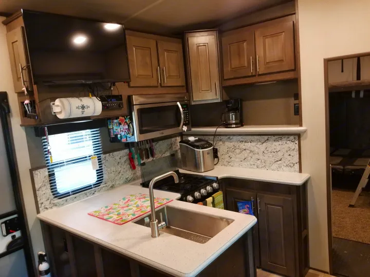 RV rental: Modern travel trailer kitchen with dark wood cabinets, microwave, sink, stove, and wall-mounted TV.. Other Other 2019