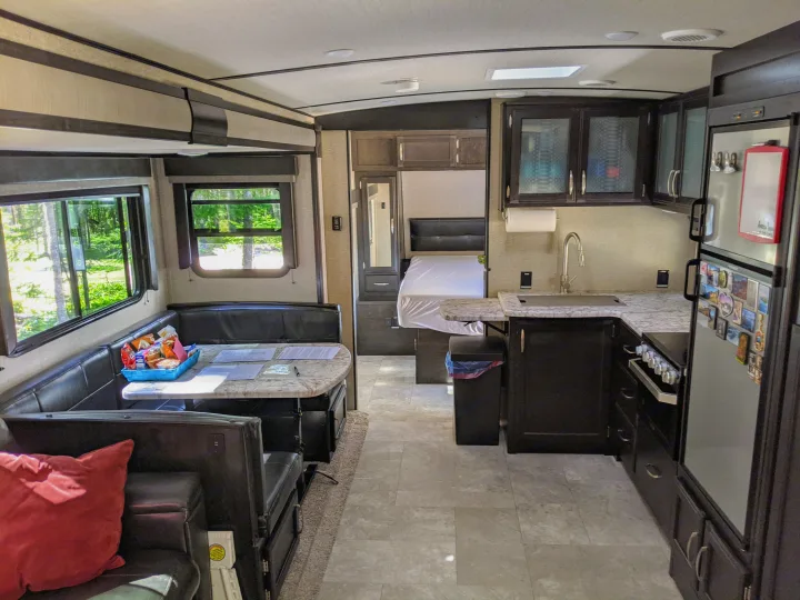 An RV rental's spacious interior: dinette with table, full kitchen, and bed, all lit by large windows.. Grand Design Imagine 2019