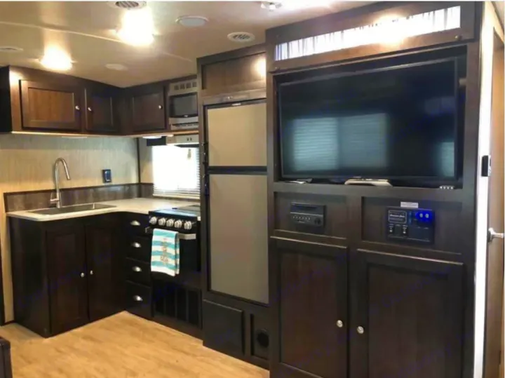 An RV rental kitchen and living area with dark wood cabinets, a TV, and modern appliances.. Cruiser Rv Corp Shadow Cruiser 2018