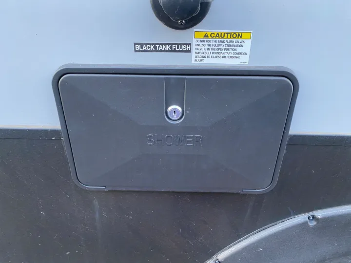 Close-up of an RV rental exterior, showing a locked outdoor shower panel and a black tank flush port with a warning.. Forest River Other 2020