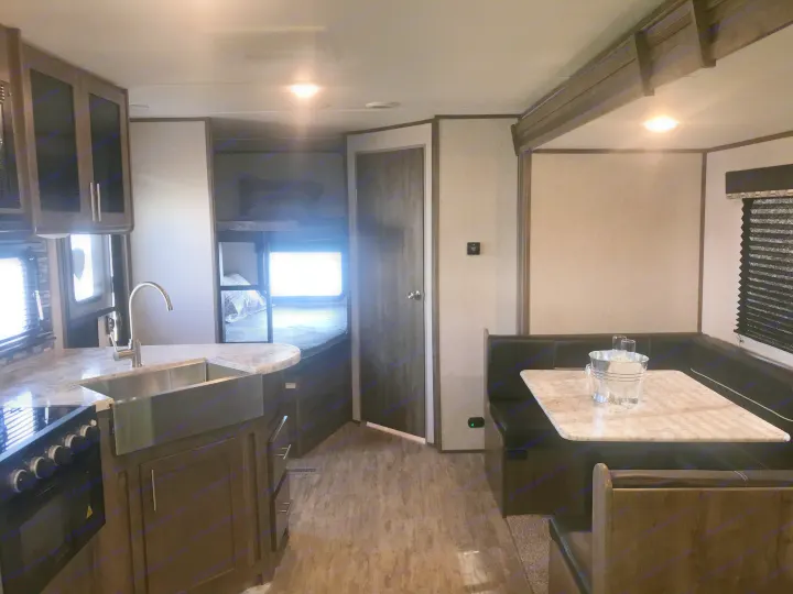 View inside a modern rv rental, showing a kitchen with sink, dining area with dinette, and bunk bed space.. Dutchmen Aspen Trail 2021