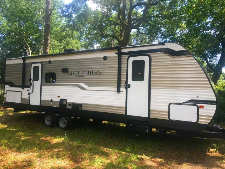 Aspen Trail RV rental. This travel trailer is ready for your outdoor adventures, parked on grass beneath tall trees.. Dutchmen Aspen Trail 2021