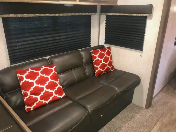 RV rental living area: brown sofa, red pillows, and black window blinds for privacy. Enjoy your trip!. Dutchmen Aspen Trail 2021