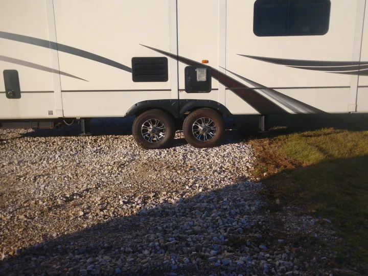 Side of a white RV rental parked on gravel. Shows dual wheels, access panels, and design details.. Montana Paramount Edition 2014