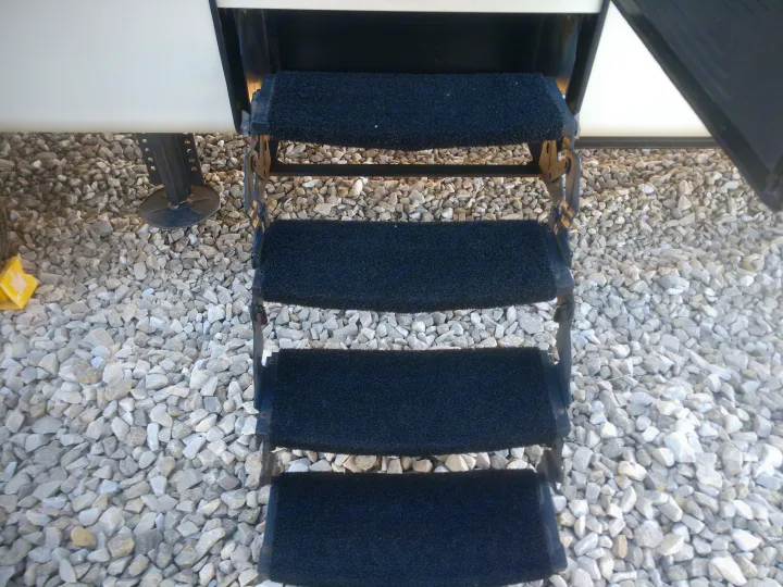Fold-out RV steps with black non-slip mats extend to a gravel surface, common for an rv rental.. Montana Paramount Edition 2014