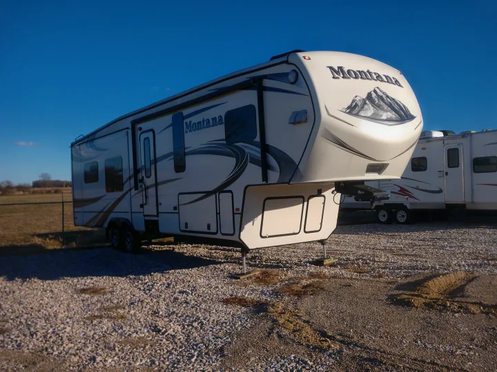 A large, white Montana fifth-wheel RV parked on a gravel lot under a clear sky. Consider this for your next rv rental.. Montana Paramount Edition 2014