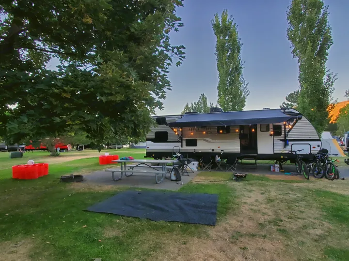 Enjoying an RV rental at a spacious campsite, complete with a picnic area, grill, and bikes under the shade trees.. Dutchmen Aspen Trail 2020