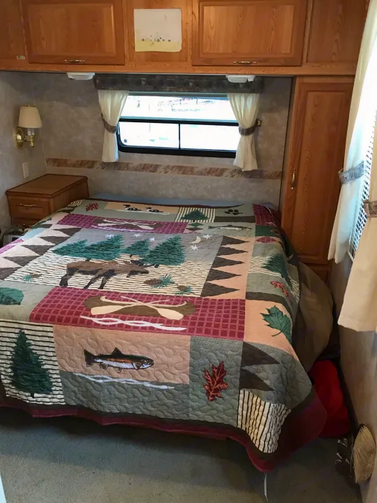 Cozy RV rental bedroom featuring a wilderness-themed quilt, wooden cabinets, and window.. Sunline Solaris/Delivery&Set-up 2002
