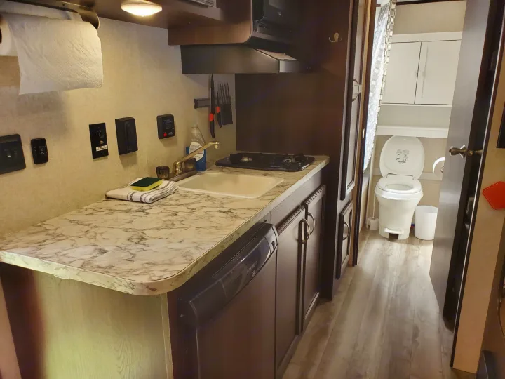 RV rental interior: Kitchenette with stove, sink, and microwave; small bathroom with toilet visible beyond.. Jayco Jay Flight 2018