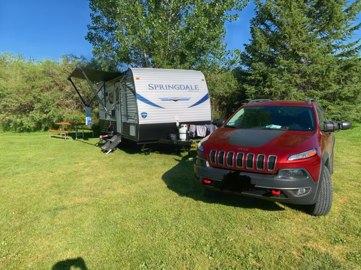 A red Jeep and a Springdale RV are set up at a sunny, grassy campsite, ideal for an rv rental adventure.. Keystone Springdale 2021