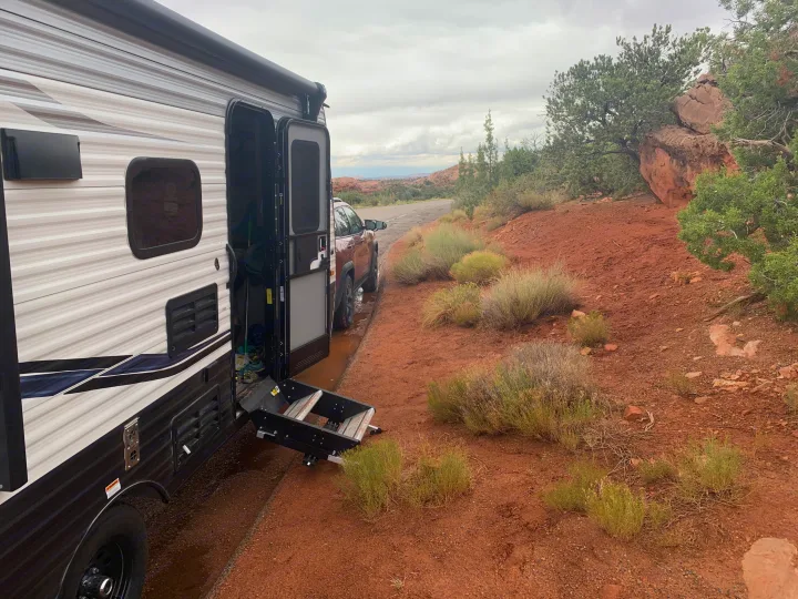 An RV rental is parked with its steps extended on a muddy red dirt pull-off, with a car and desert scenery.. Keystone Springdale 2021