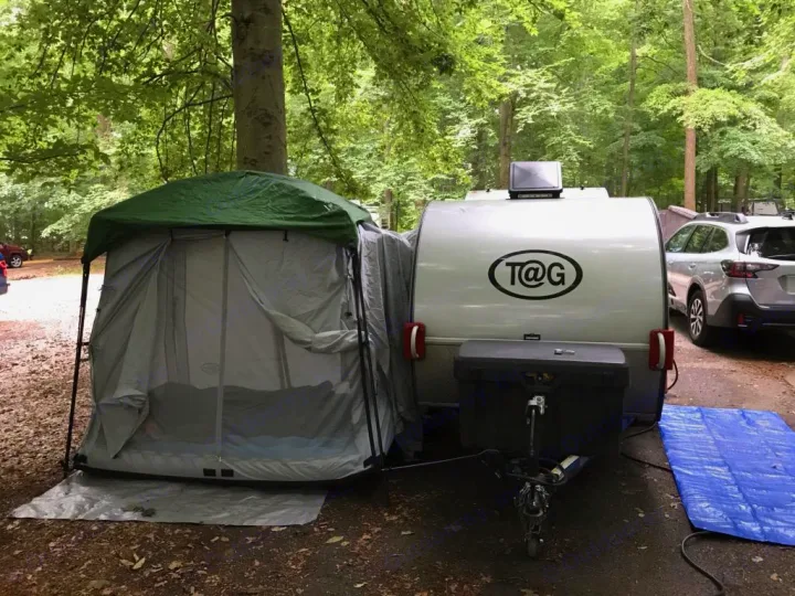 This T@G teardrop camper RV rental, with attached tent, is set up for camping at a wooded campsite.. T@G T@G Trailer 2016