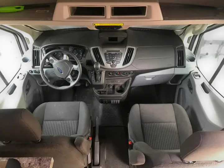 RV rental van's spacious front cabin, showing dashboard, steering wheel, front seats, and overhead storage.. Ford Transit Custom 2015