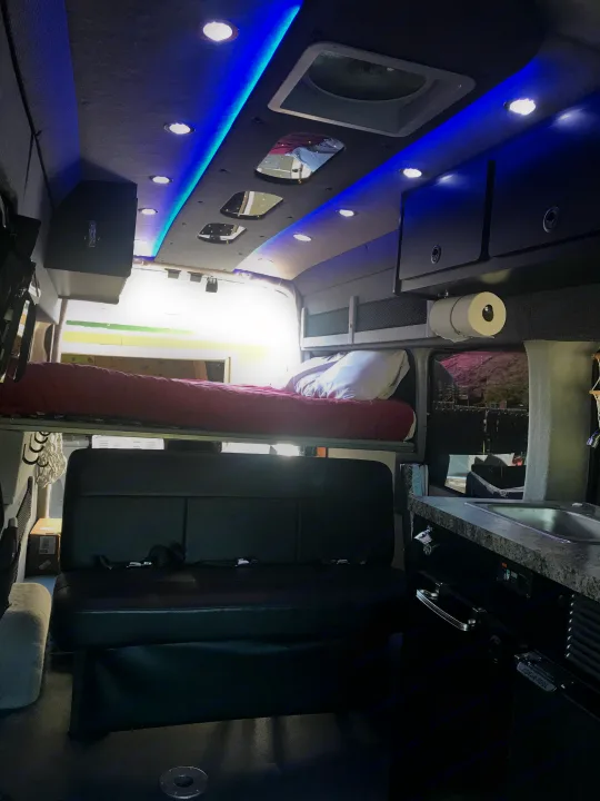 Compact RV rental interior featuring blue LED lighting, a convertible bed, and small kitchen setup for comfortable travel.. Ford Transit Custom 2015