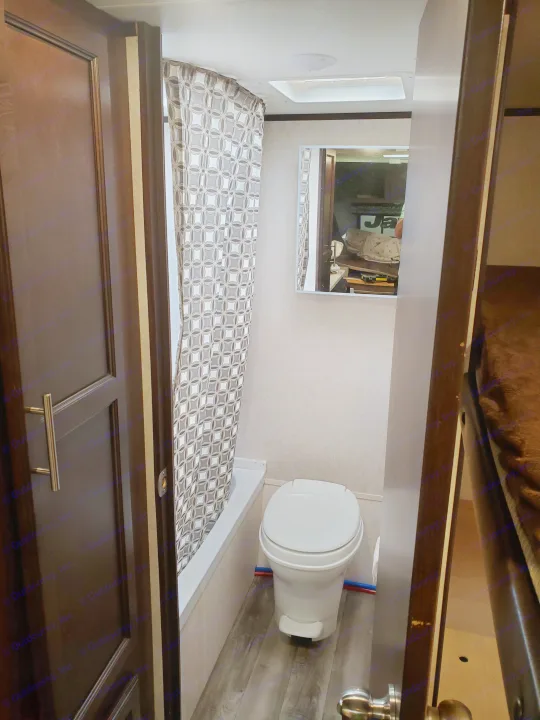 Inside an RV rental bathroom, featuring a compact toilet, shower/tub, and mirror reflecting the living space.. Jayco Jay Flight 2019