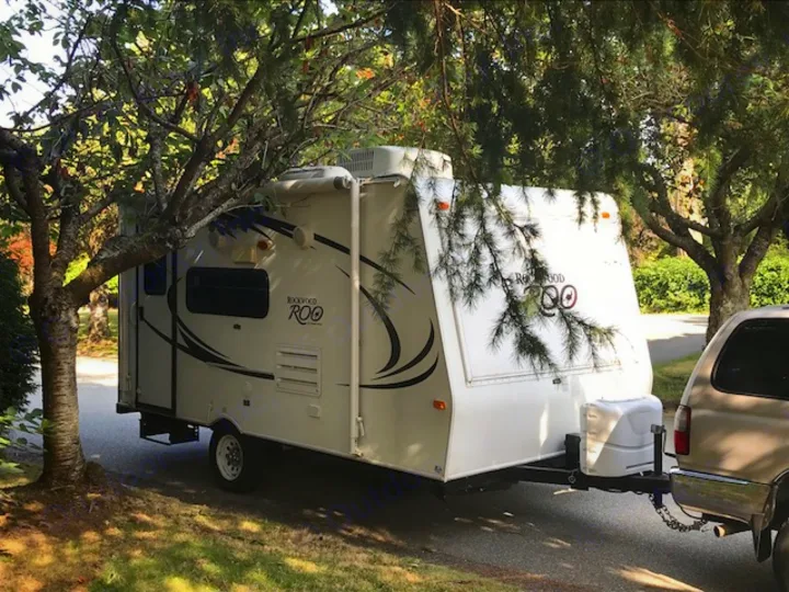 Experience the outdoors! A white Rockwood Roo RV rental travel trailer, hitched to an SUV, parked under lush trees.. Rockwood Roo 2011