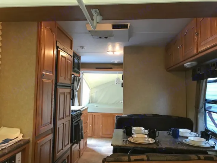 Inside a comfortable RV rental, showing a full kitchen, dining area set with dishes, and a rear pop-out bed.. Rockwood Roo 2011