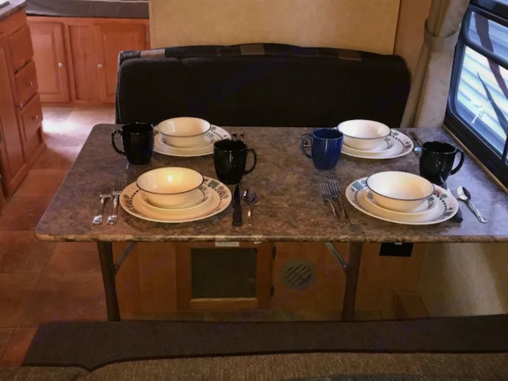 RV rental interior: dining table set for four with plates, bowls, mugs, and cutlery in a cozy camper setting.. Rockwood Roo 2011