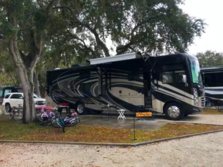 Spacious RV rental with extended awning and bikes, set up at a shaded campsite, ready for outdoor travel.. Thor Motor Coach Challenger 2018