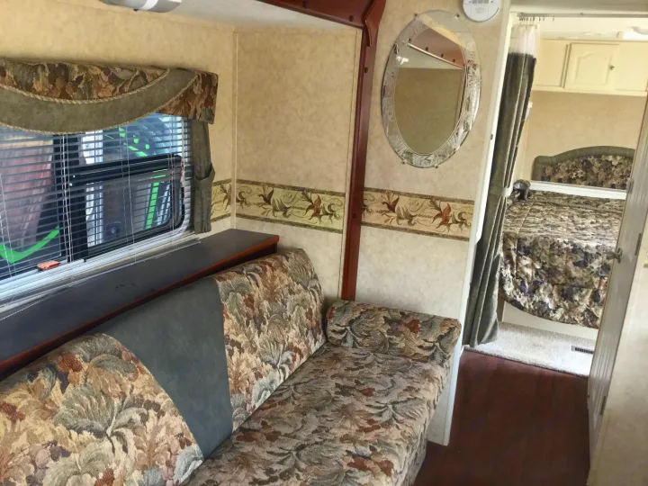 Spacious RV rental interior featuring a floral-patterned couch, window with valance, mirror, and a cozy bedroom.. Max Lite ML26RK 2006