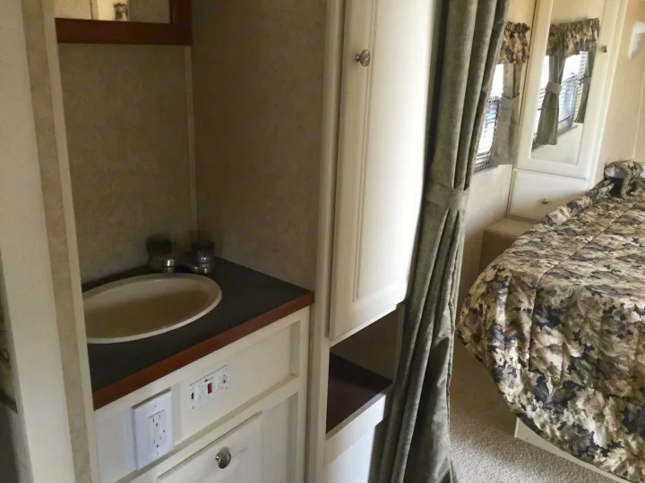 Inside this RV rental: a compact living space with a sink, control panel, and a bedroom featuring a mirrored cabinet and patterned bedding.. Max Lite ML26RK 2006
