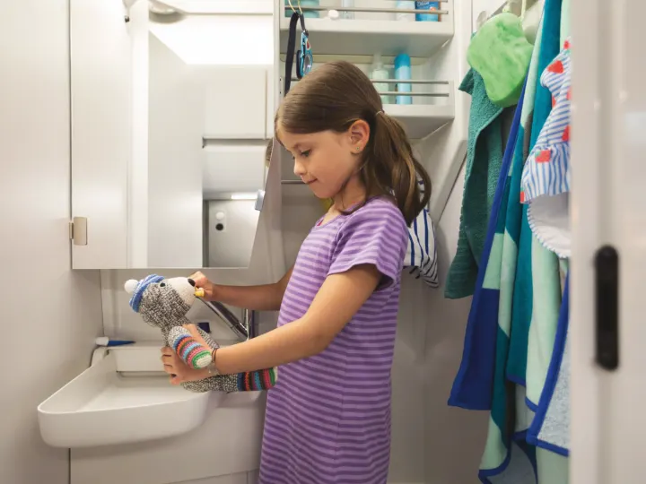 RV rental: A young girl helps her sock monkey 'brush its teeth' at the sink in the compact bathroom.. Volkswagen Grand California 600 2020