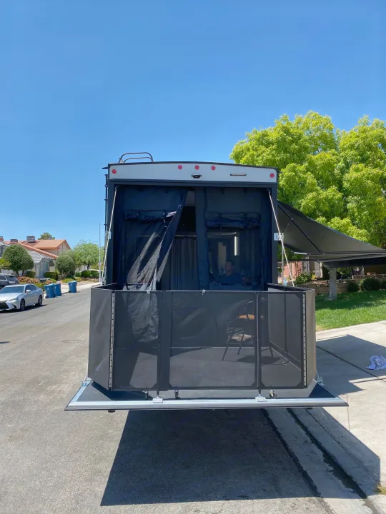 Rear view of an RV rental with a unique patio deck setup and mesh enclosure for outdoor living, parked on a sunny street.. Forest River Xlr Thunrderbolt 2020