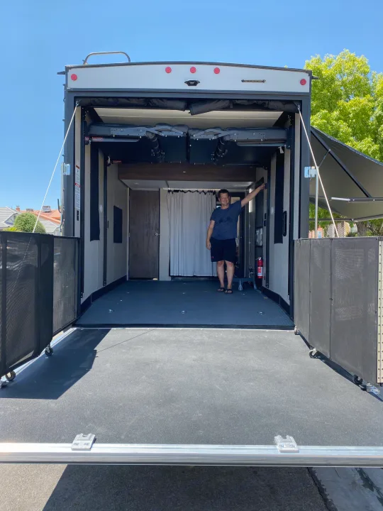 Man inside an RV rental toy hauler with its rear ramp down, creating an outdoor deck. The spacious interior is visible.. Forest River Xlr Thunrderbolt 2020